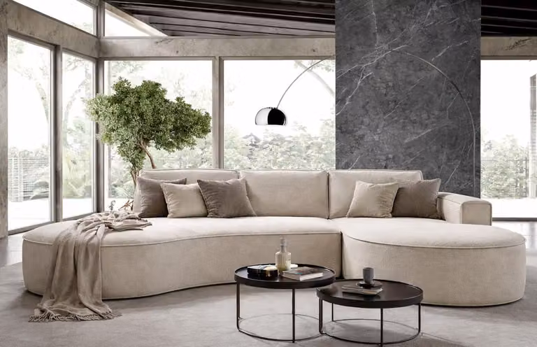 Divano angolare GUTTO MOLLY, con forma arrotondata, rivestito in tessuto morbido color crema, beige e grigio chiaro – un design moderno e di tendenza! Novità 2025 (con funzione letto)