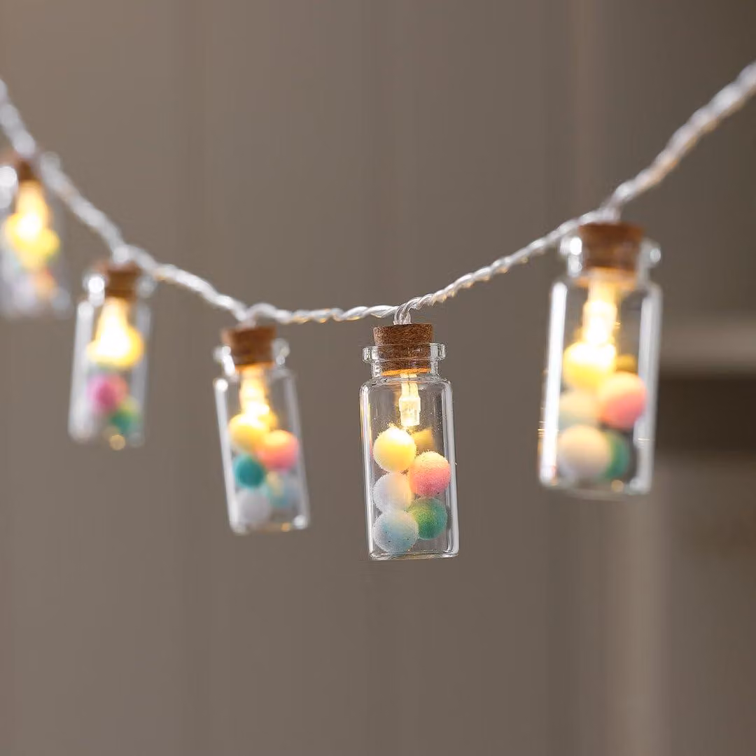 Catena luminosa con 10 lampadine in vetro, pompon color pastello, luci LED bianco caldo e timer