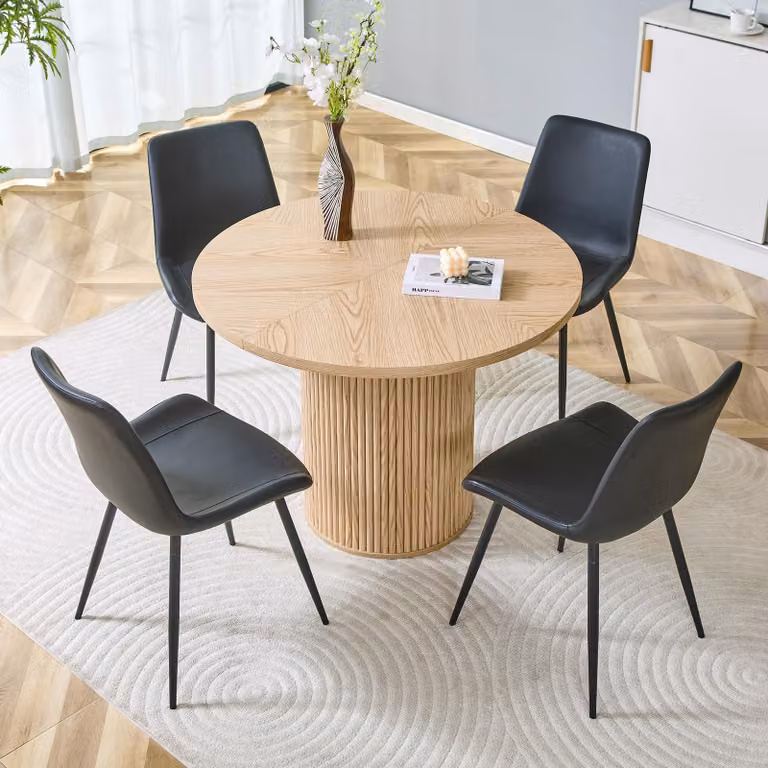 Set da pranzo STILVORA, composto da 1 tavolo e 4 sedie. Il tavolo, con un diametro di 100 cm, presenta un aspetto in legno chiaro. Il set include anche 4 sedie rivestite in ecopelle nera