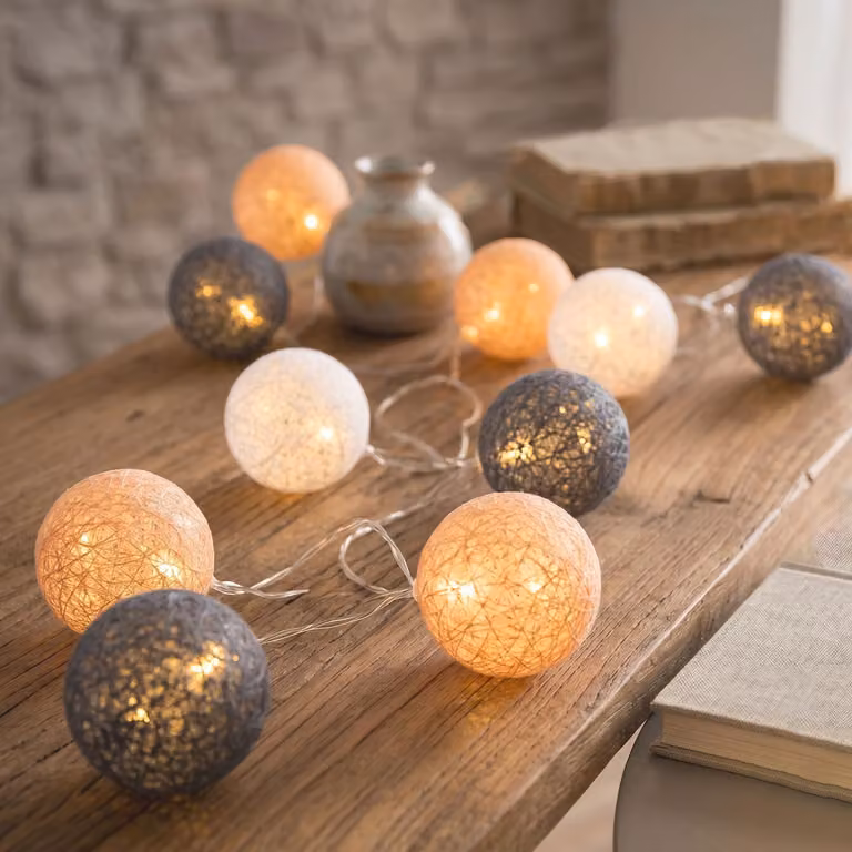 Catena luminosa con 10 luci a LED, composta da sfere, lanterne e elementi in cotone, nei colori arancione e bianco. Luce calda, ideale per la decorazione