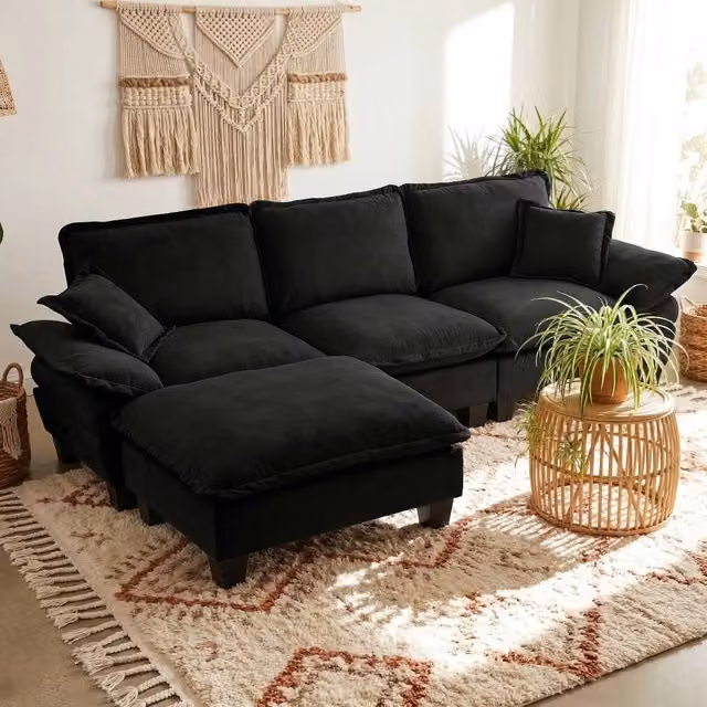 Divano angolare a L Mivray in velluto nero con pouf e cuscini coordinati, struttura in legno massello e design reversibile per il tuo soggiorno